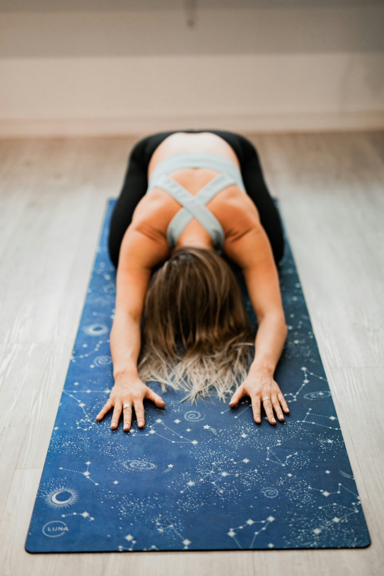 Eine Frau praktiziert auf einer mit Sternbildern bedruckten Yogamatte eine Yin-Yoga-Dehnung, bei der sie ihren Oberkörper nach vorne über ihre ausgestreckten Beine beugt. Die Pose fördert Entspannung und Erdung, was in Yin Yoga Online-Sitzungen angestrebt wird.
