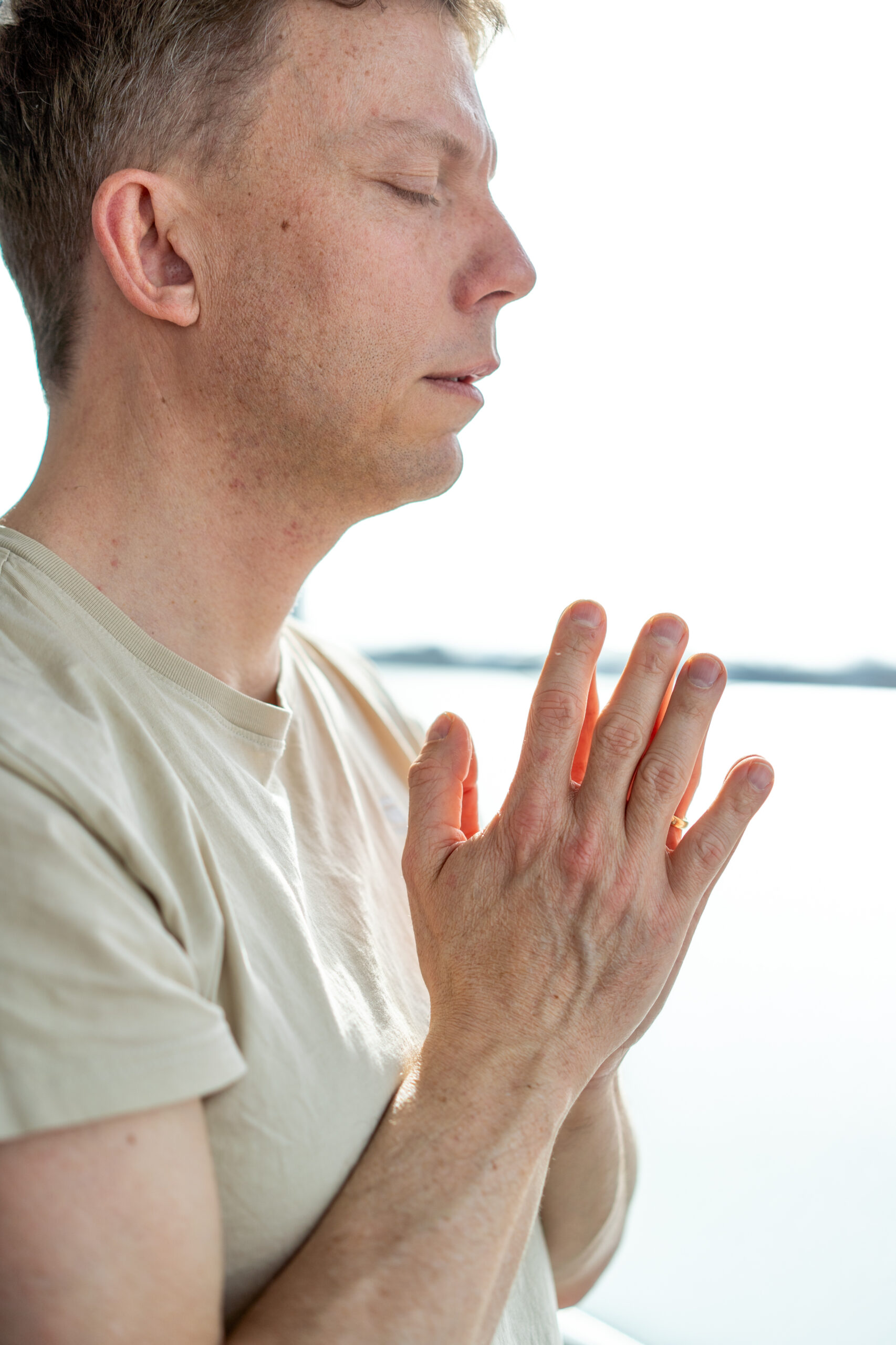 Ein Mann mit geschlossenen Augen in einer Yoga-Pose, seine Hände in einer Geste des Gleichgewichts und der Konzentration vor seinem Herzen, was auf die tiefe Verbindung und Ruhe hinweist, die in einer Yin-Yoga-Ausbildung gelehrt wird.