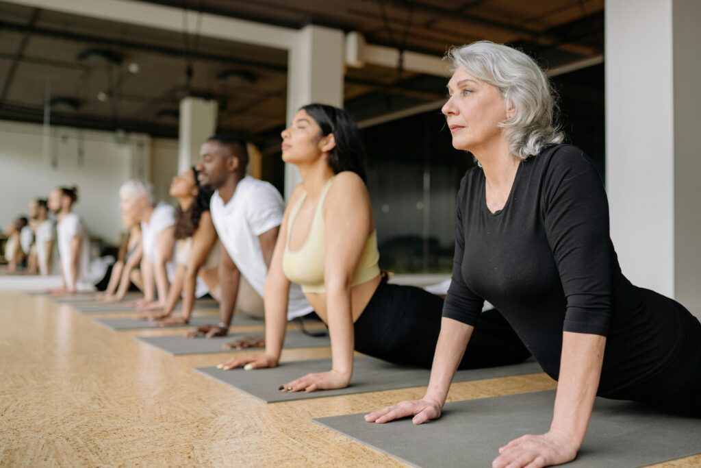 Diverse Gruppe von Yin Yoga Anfängern in Hamburg praktiziert die Kobra-Haltung auf Matten, geleitet von einer erfahrenen Seniorin im Vordergrund