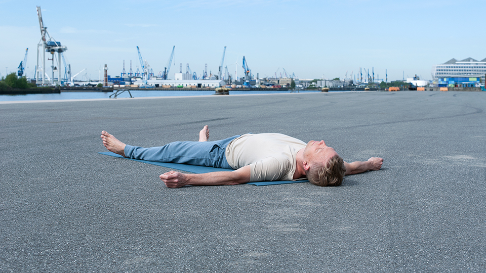 Jan Wolk in Shavasana auf der Yoga-Matte, im Hintergrund die Hamburger Hafenkräne
